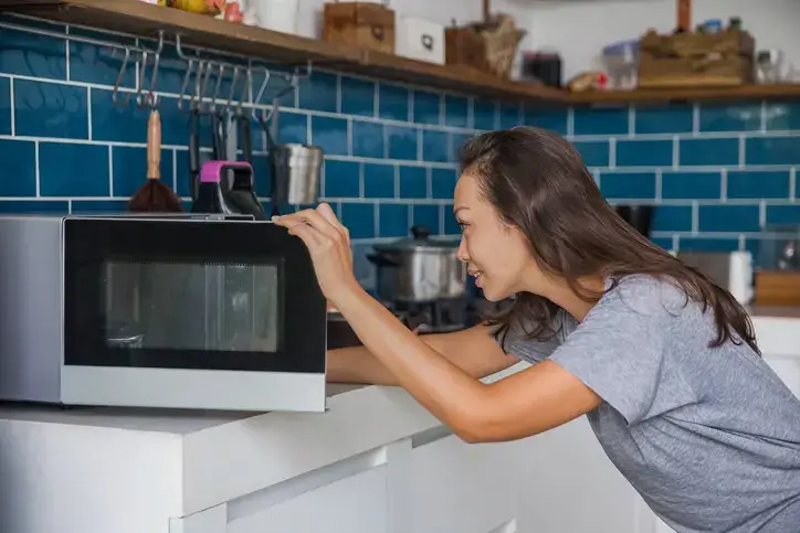 Beautiful Asian woman reheating her meals inside microwave.