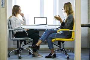 Young female employee discussing working details with her administrative executive during informal meeting in coworking office sitting near modern laptop computer with mock up screen connected to wifi