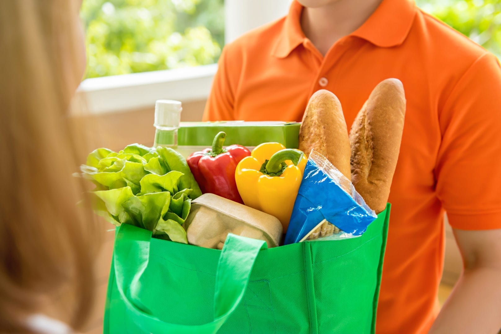 The Best Mobile Apps for Travel Nurses Grocery store delivey man wearing orange polo-shirt delivering food to a woman at home