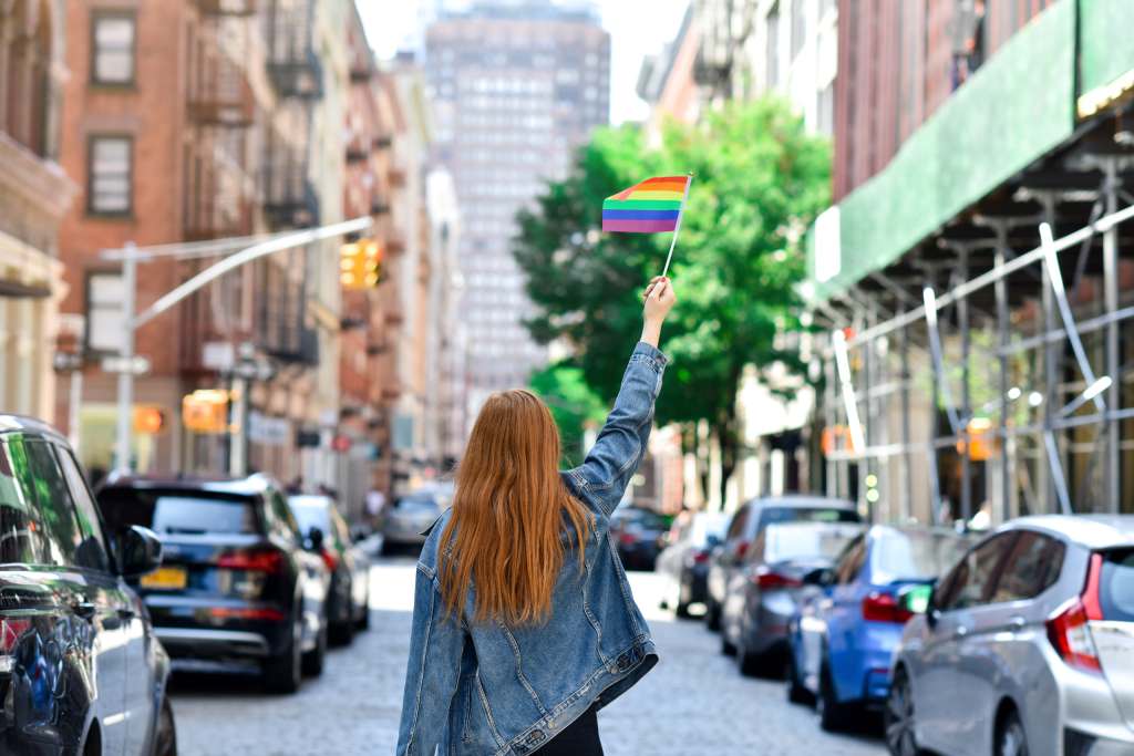 Woman holding a rainbow Pride flag in New York City, showing LGBTQ+ pride and visibility in an urban setting.