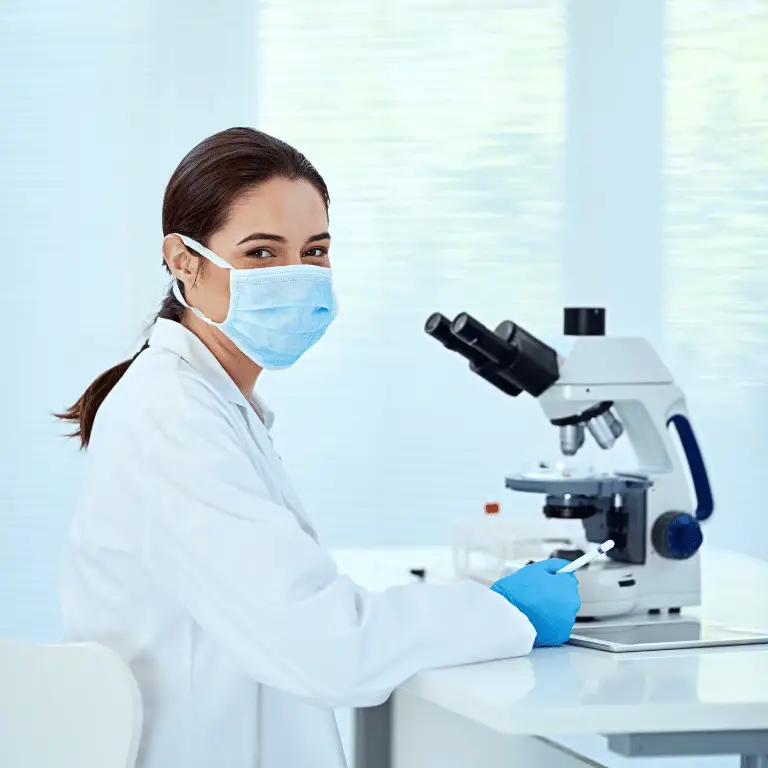 Laboratory scientist wearing protective equipment working beside a microscope in a clinical lab.